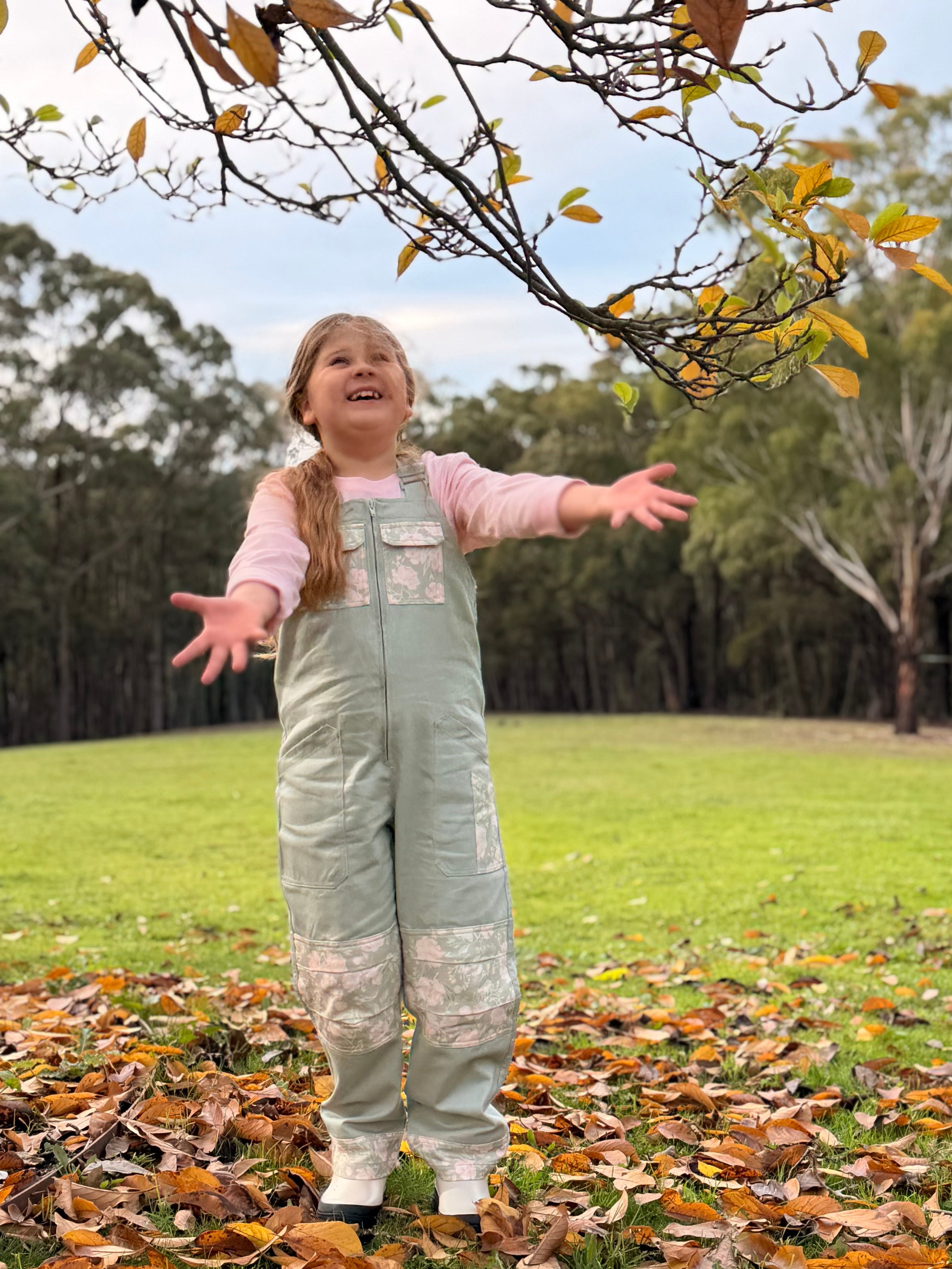 Girl in Lil' Patch Dungarees throwing autumn leaves in the air